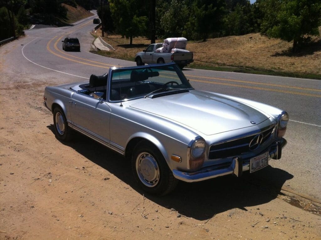 Classic silver convertible parked on a sunny road.