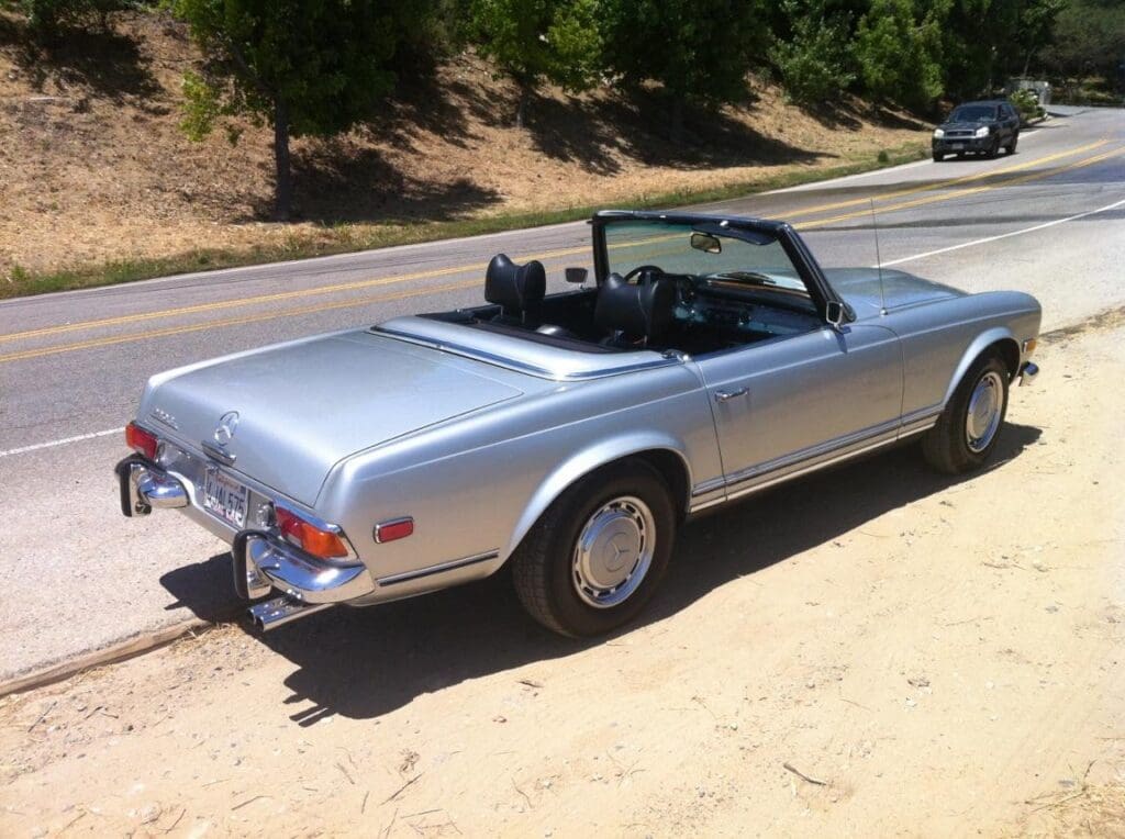Classic silver convertible car parked on a sunny dirt road.