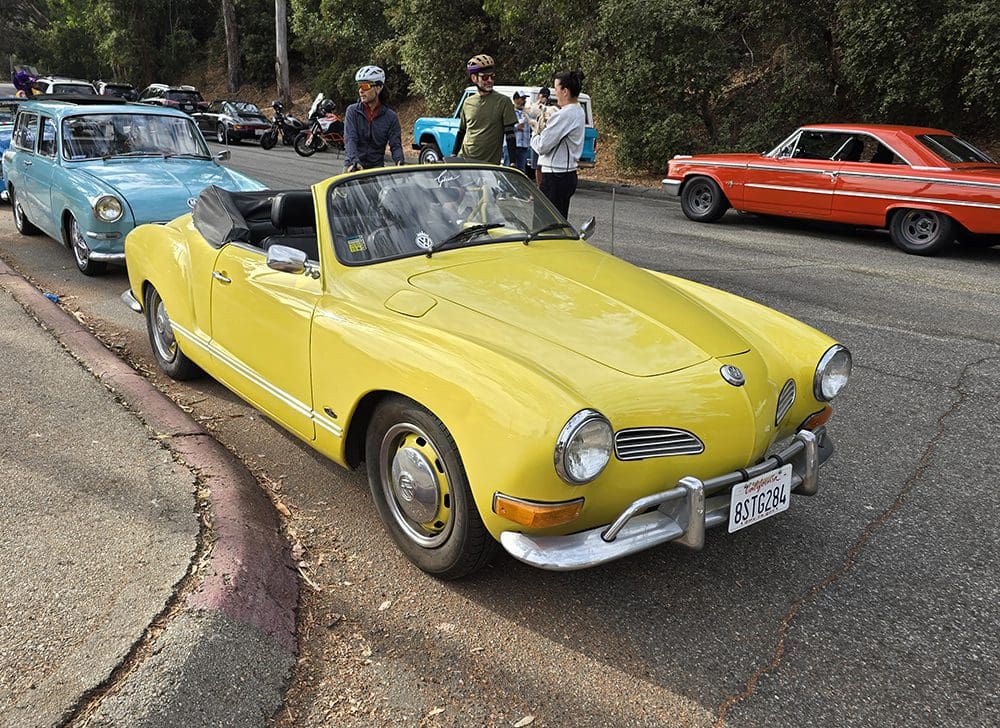 Yellow vintage convertible car parked at a car show with people around.