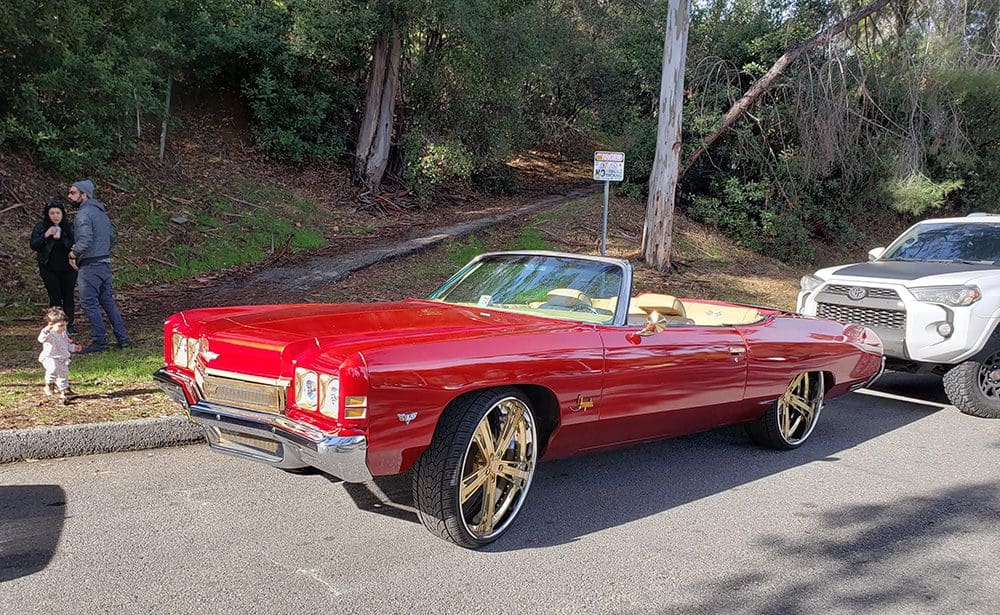 Classic red convertible car with gold rims parked on a sunny street.