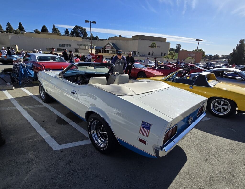Classic white convertible car parked at a car show on a sunny day.