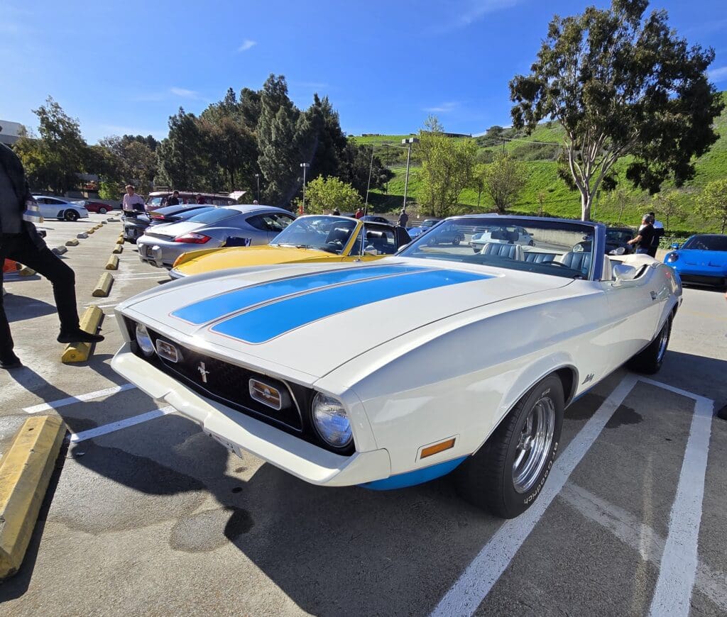 Classic white muscle car with blue racing stripes parked outdoors.
