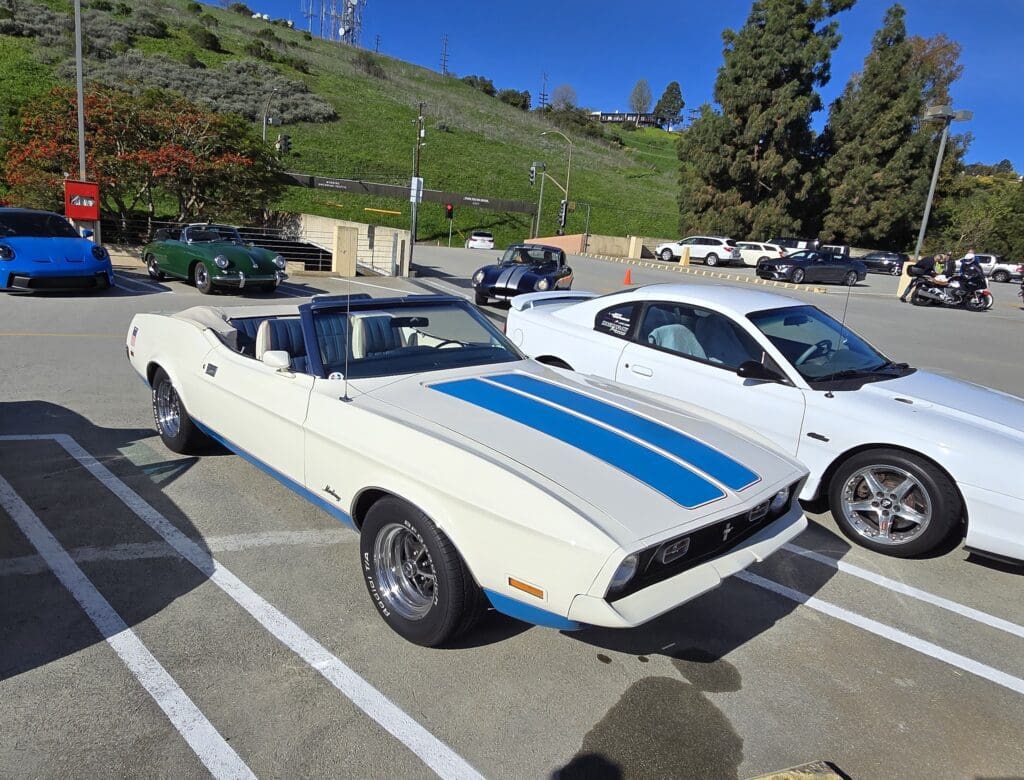 Classic white convertible muscle car with blue racing stripes parked outdoors.