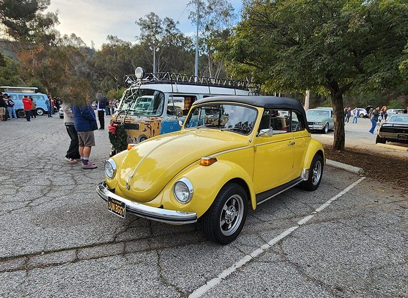 Yellow vintage Volkswagen Beetle parked outdoors with people nearby.