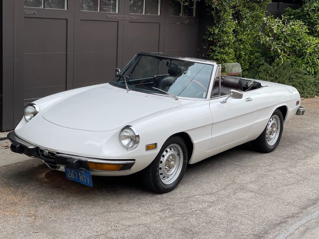 Classic white convertible car parked outdoors near greenery.