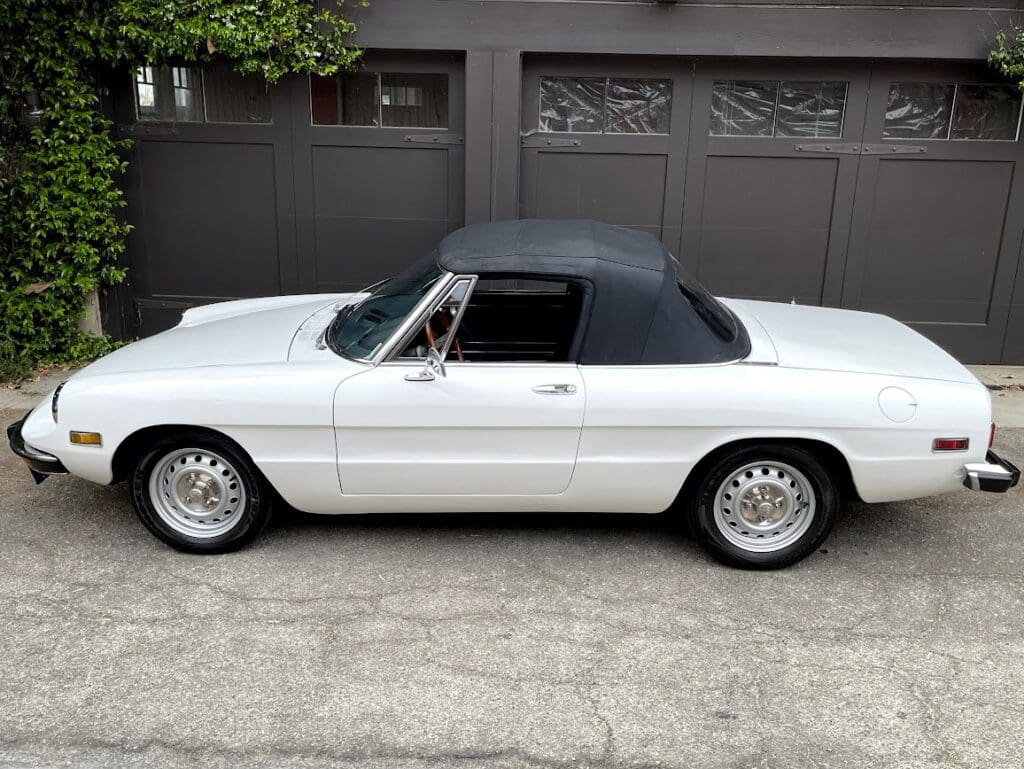 Classic white convertible car with a black soft top parked in front of garage doors.