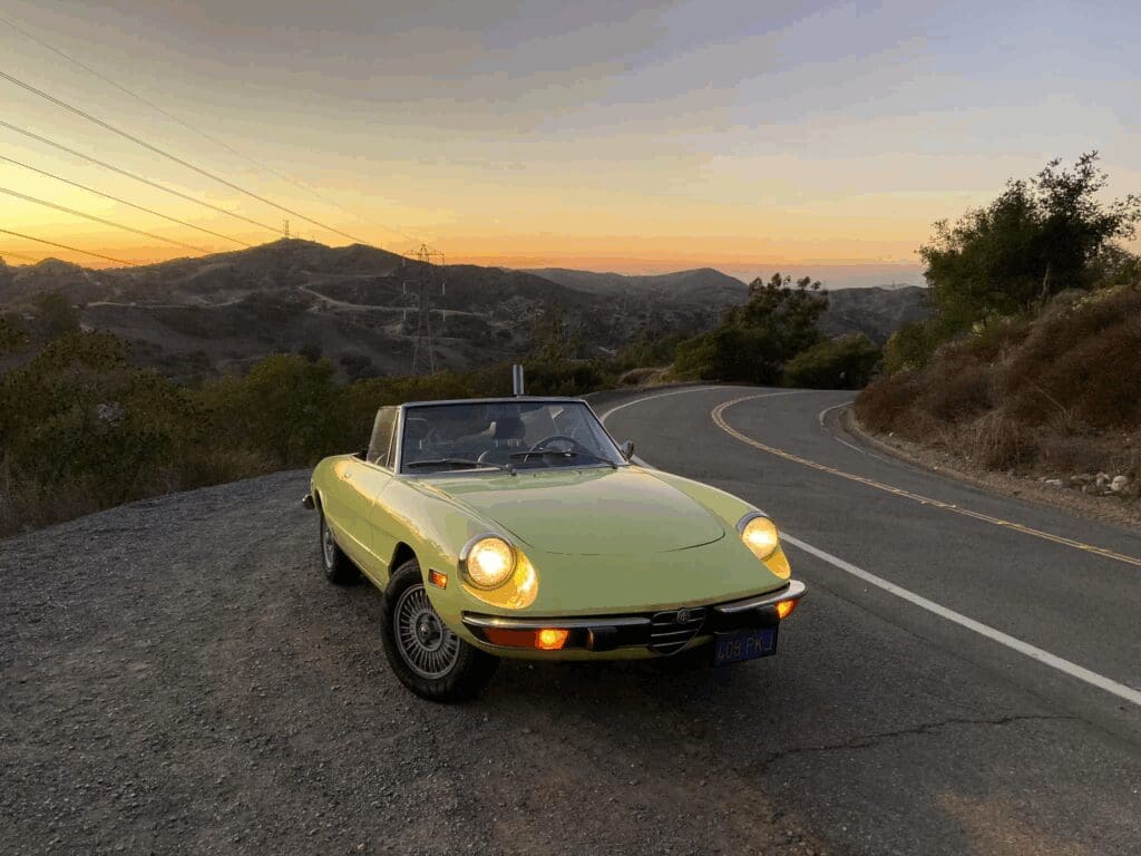 Yellow convertible car parked on a winding mountain road at sunset.