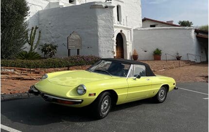 A vintage lime green convertible car parked near a white building.