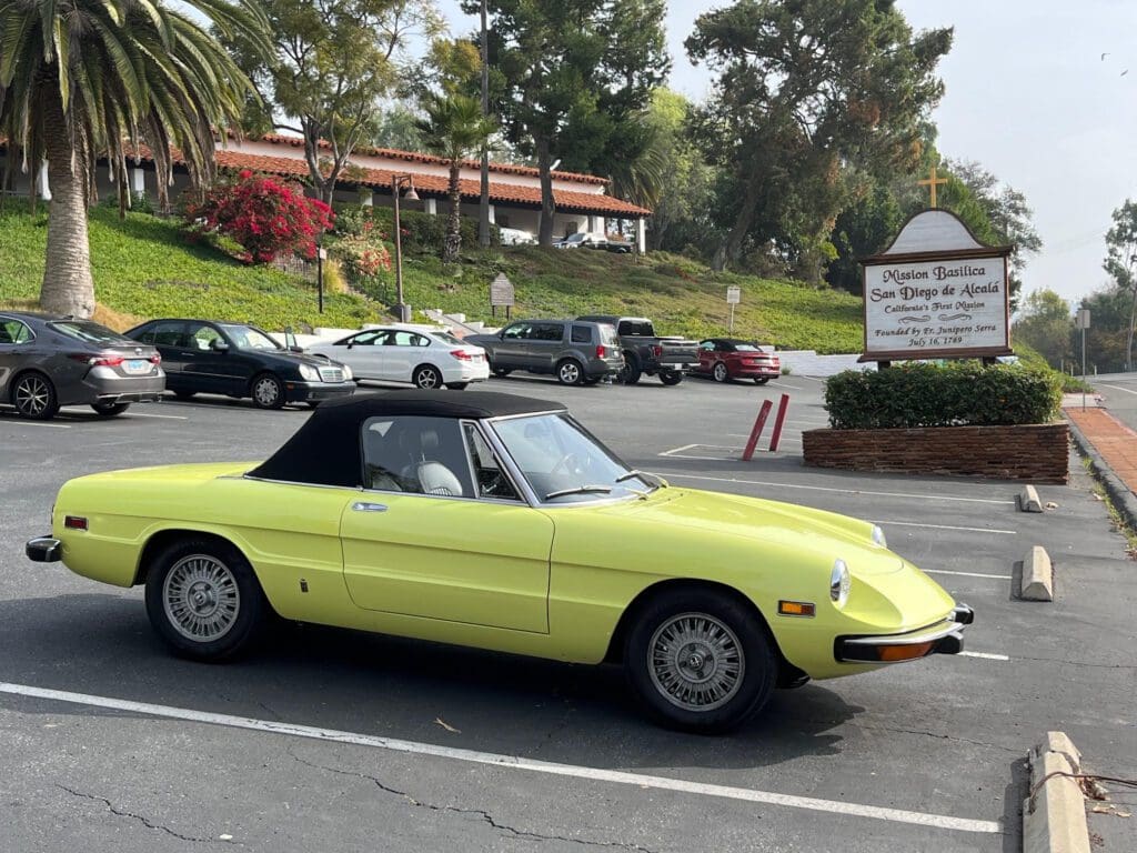 A vintage yellow convertible parked in a lot on a sunny day.