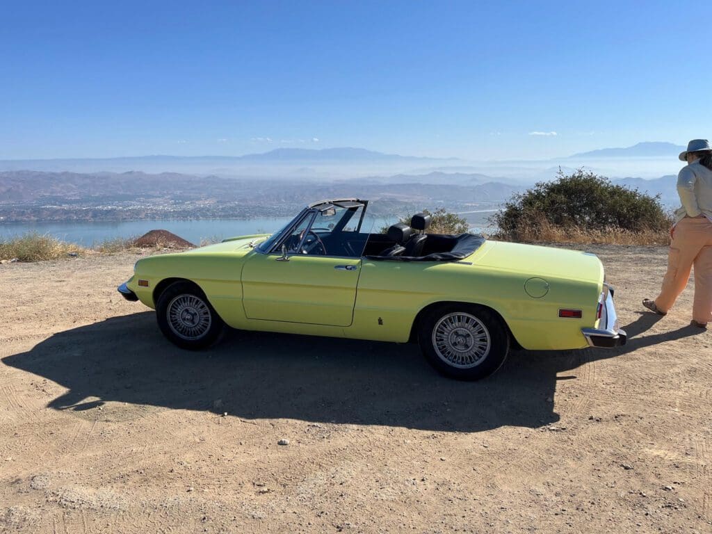 Classic yellow convertible car parked near a scenic coastal view.