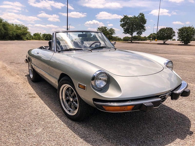 Classic silver convertible sports car parked under a blue sky.