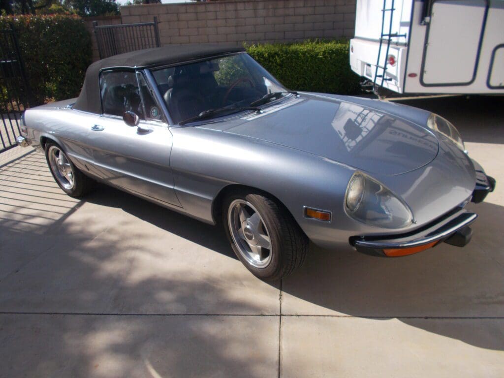 Classic silver convertible car parked on driveway under sunlight.