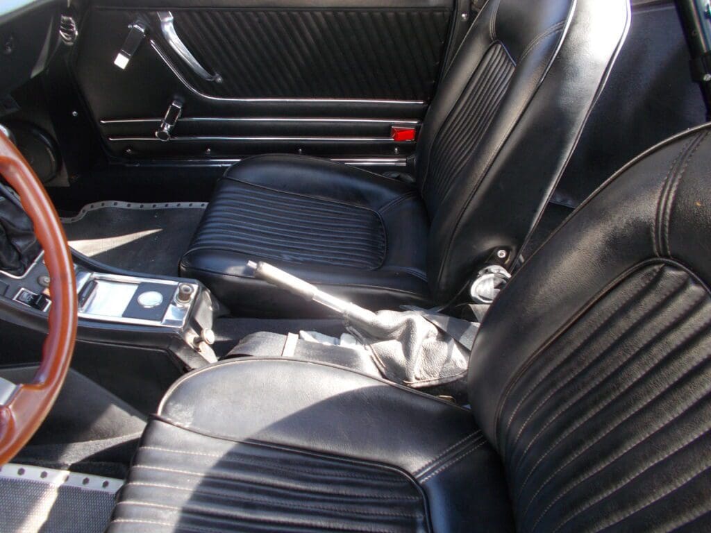 Interior of a classic car with black leather seats and manual gear shift.