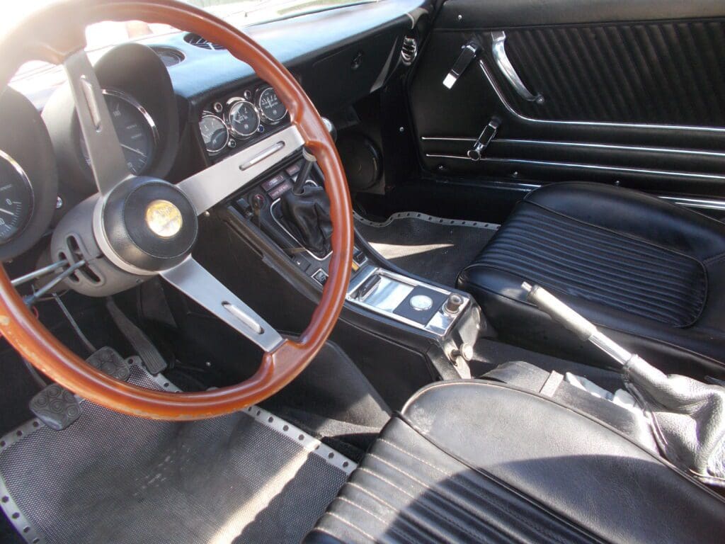 Classic car interior with wooden steering wheel and black leather seats.