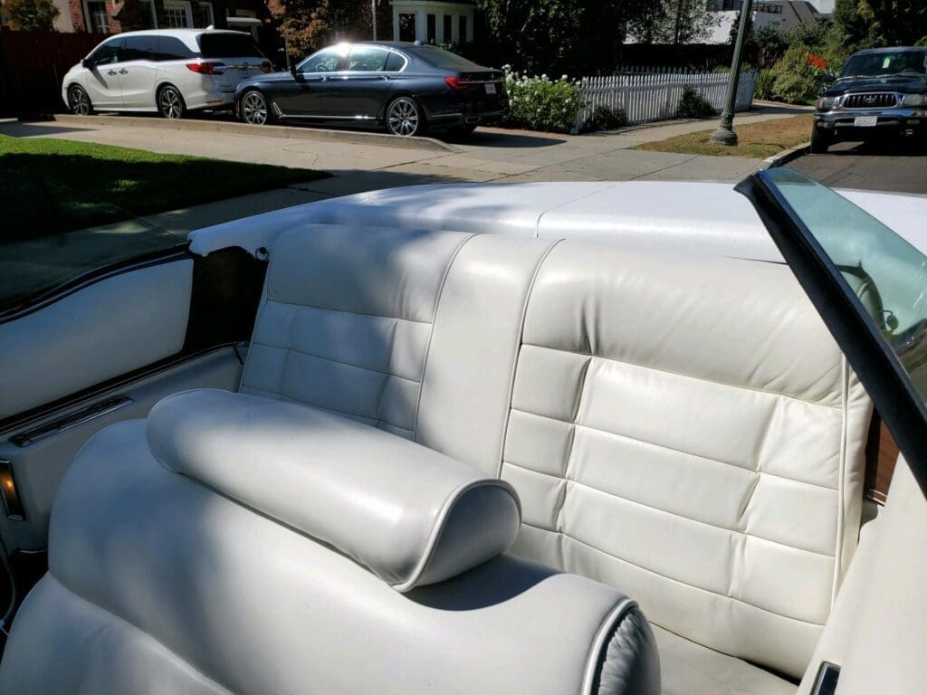 White leather interior of a convertible car with seats and headrest.