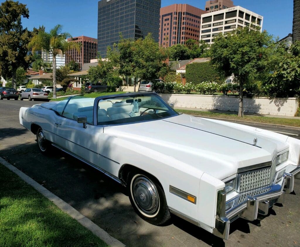 Classic white convertible car parked on a city street under a sunny sky.
