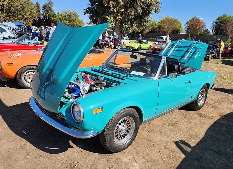 Classic turquoise convertible car with hood open at outdoor car show.