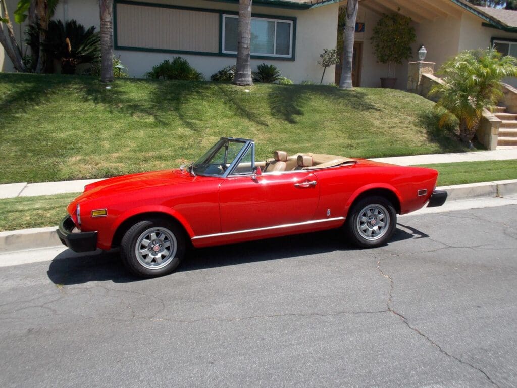 Classic red convertible parked on a sunny suburban street.