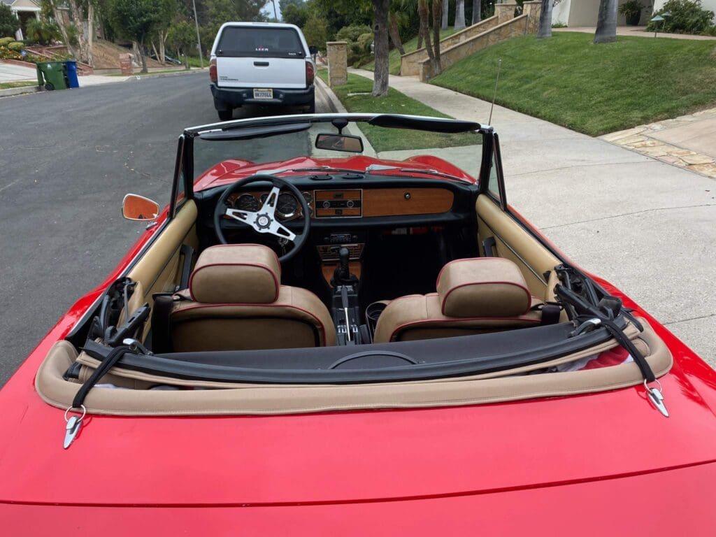 Red convertible car parked on a street with a white vehicle behind it.