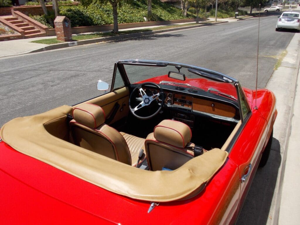 Red vintage convertible with beige interior parked on a quiet street.