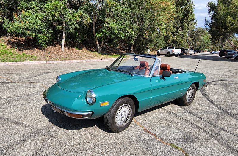 Classic green convertible car parked under trees on a sunny day.