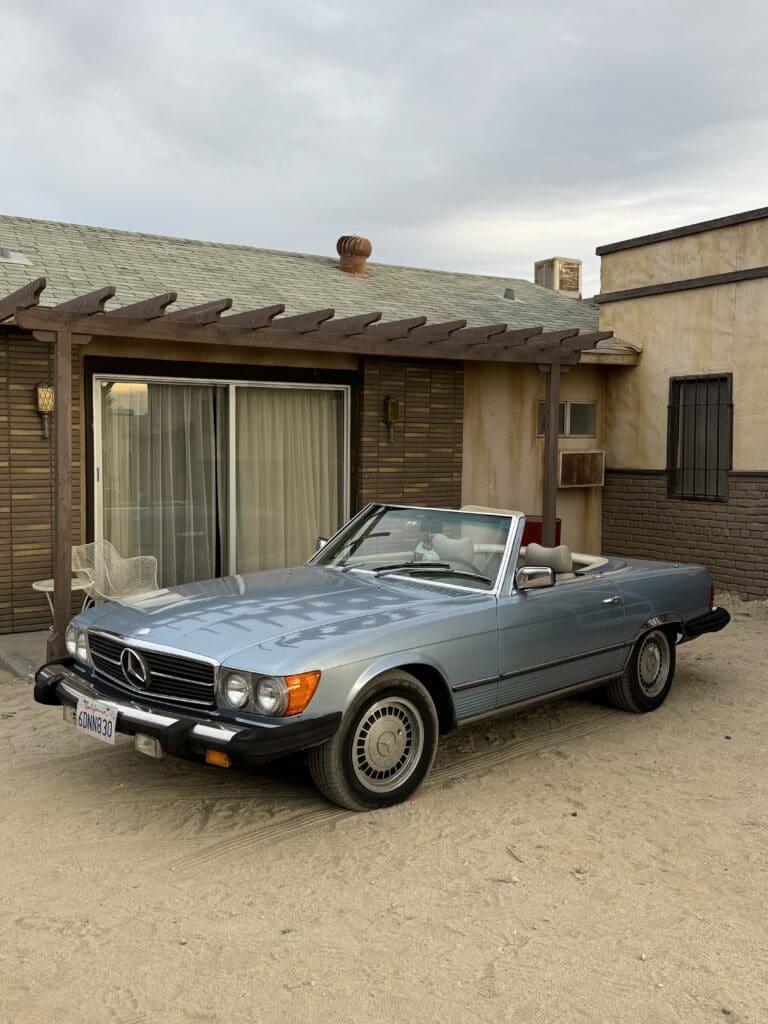 Classic blue convertible parked outside a rustic building.