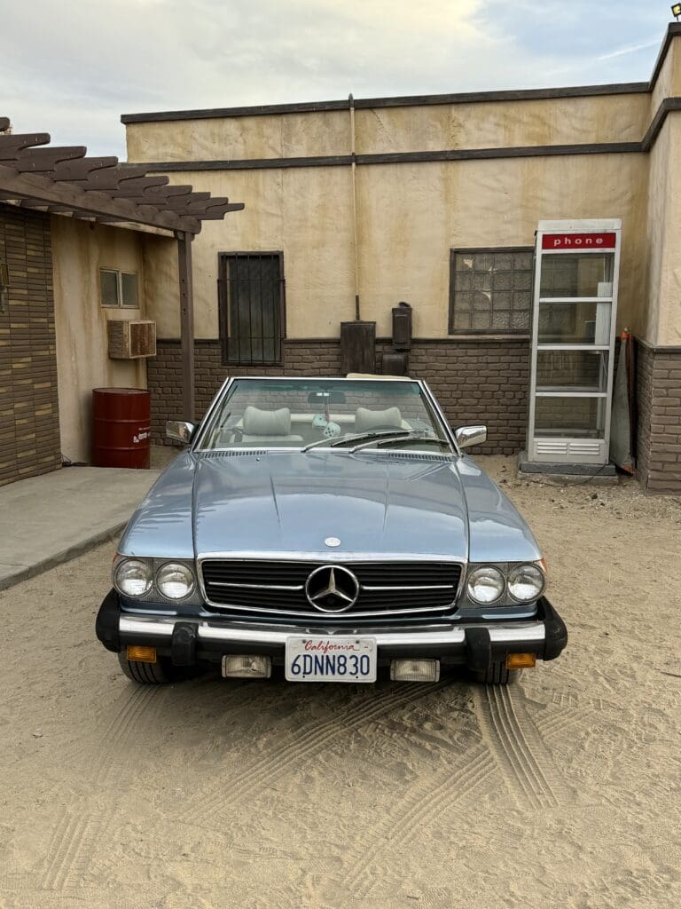 Classic blue Mercedes-Benz convertible parked in a rustic courtyard.
