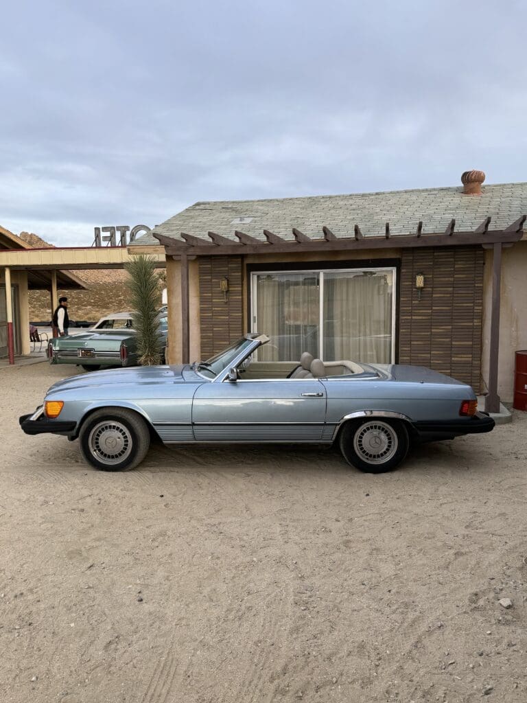 Classic blue convertible parked outside a rustic building under a cloudy sky.