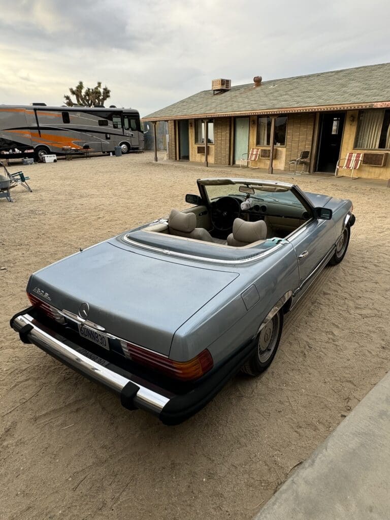Classic blue convertible car parked outside a rustic building.