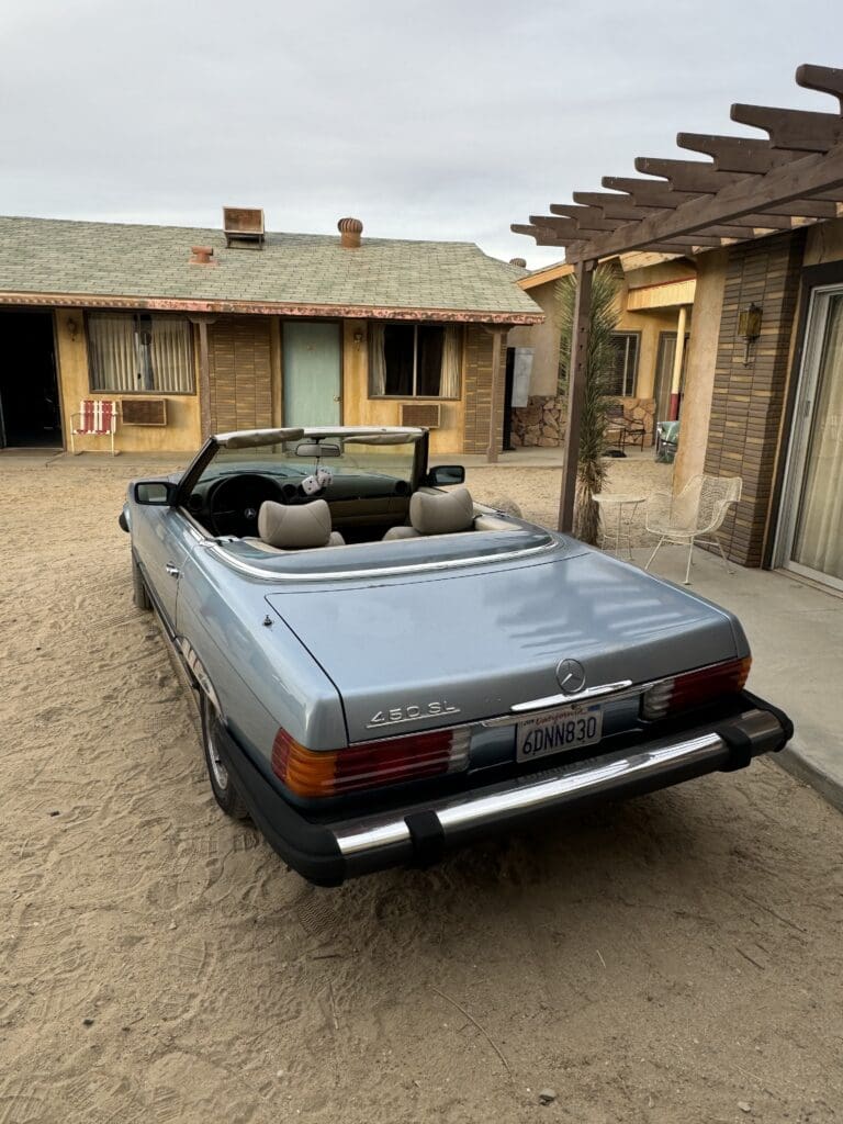 Classic blue convertible car parked in a rustic courtyard.