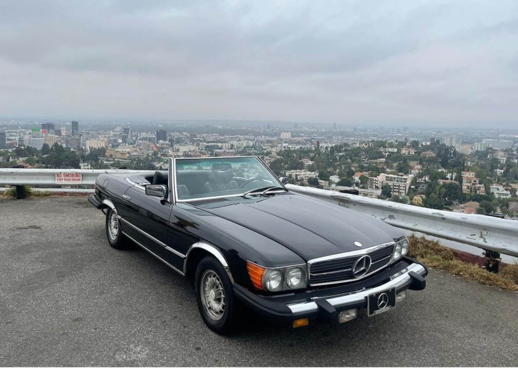 Vintage black Mercedes convertible parked with a cityscape background.