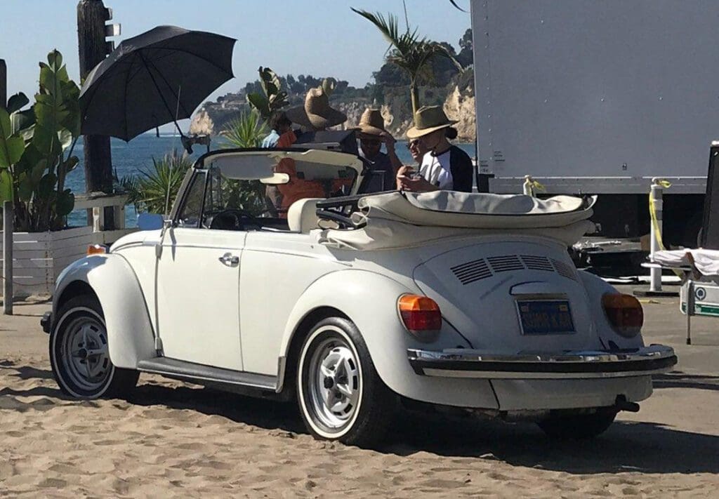 Classic white Volkswagen Beetle convertible parked on a sandy beach.