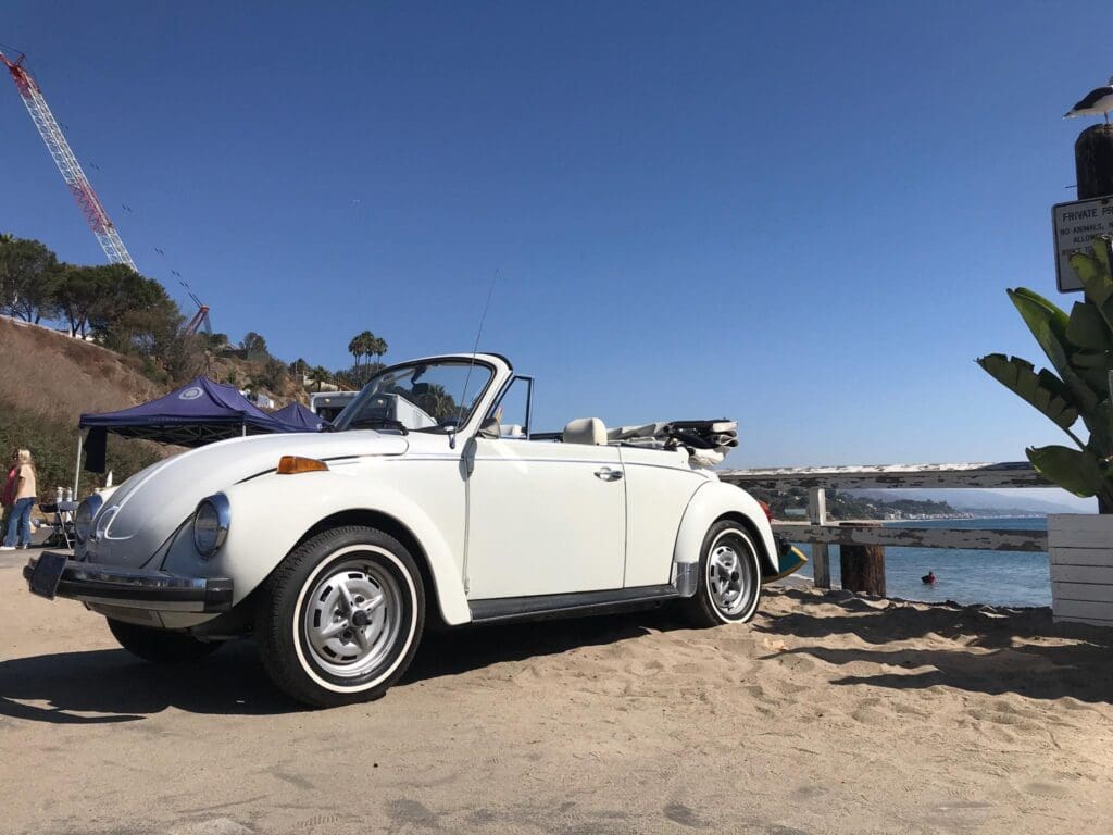 Classic white convertible car parked by the water on a sunny day.