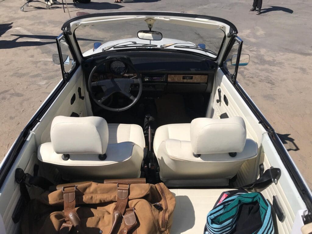 Interior view of a classic convertible car with white seats and a wooden dashboard.