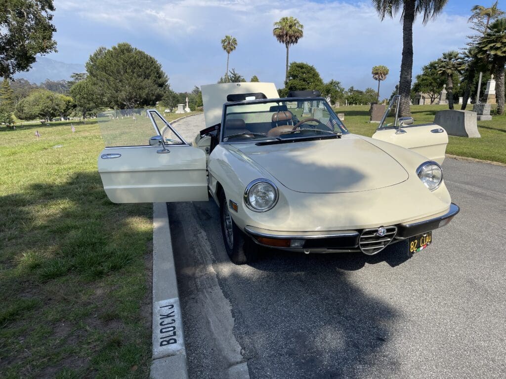 Classic white convertible parked with its door open on a sunny day.