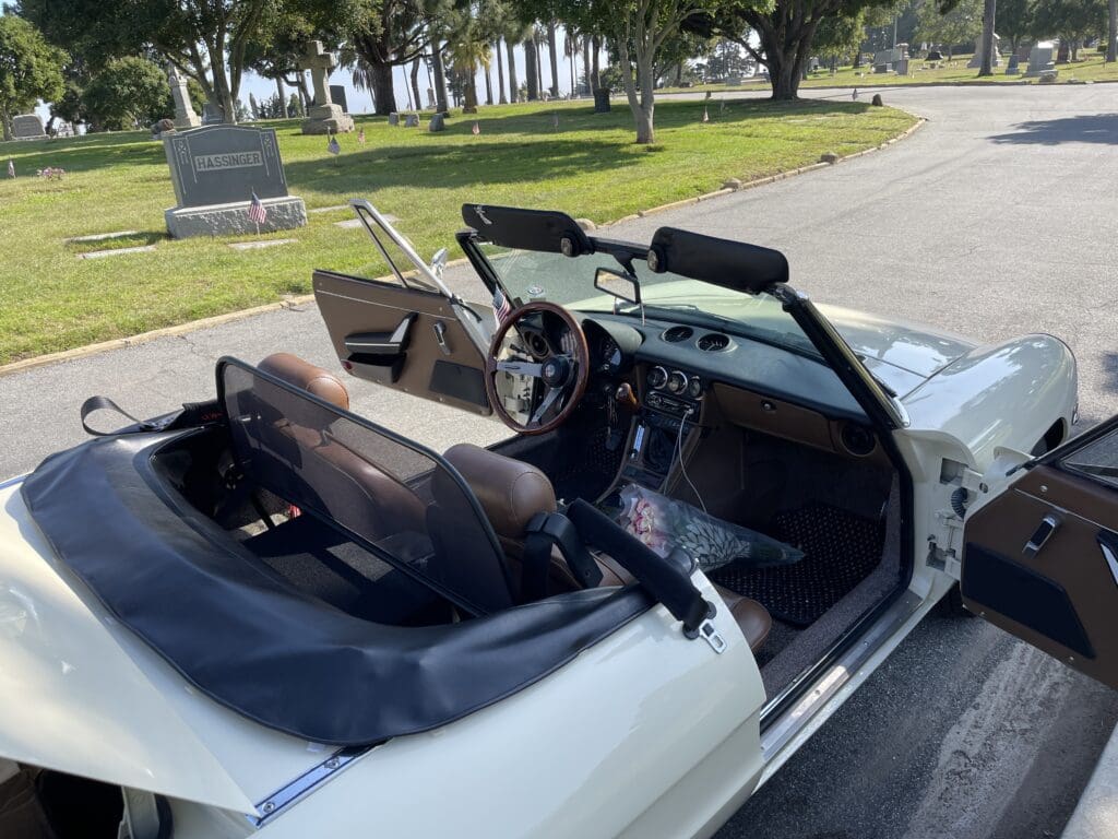 White convertible car parked near a cemetery on a sunny day.
