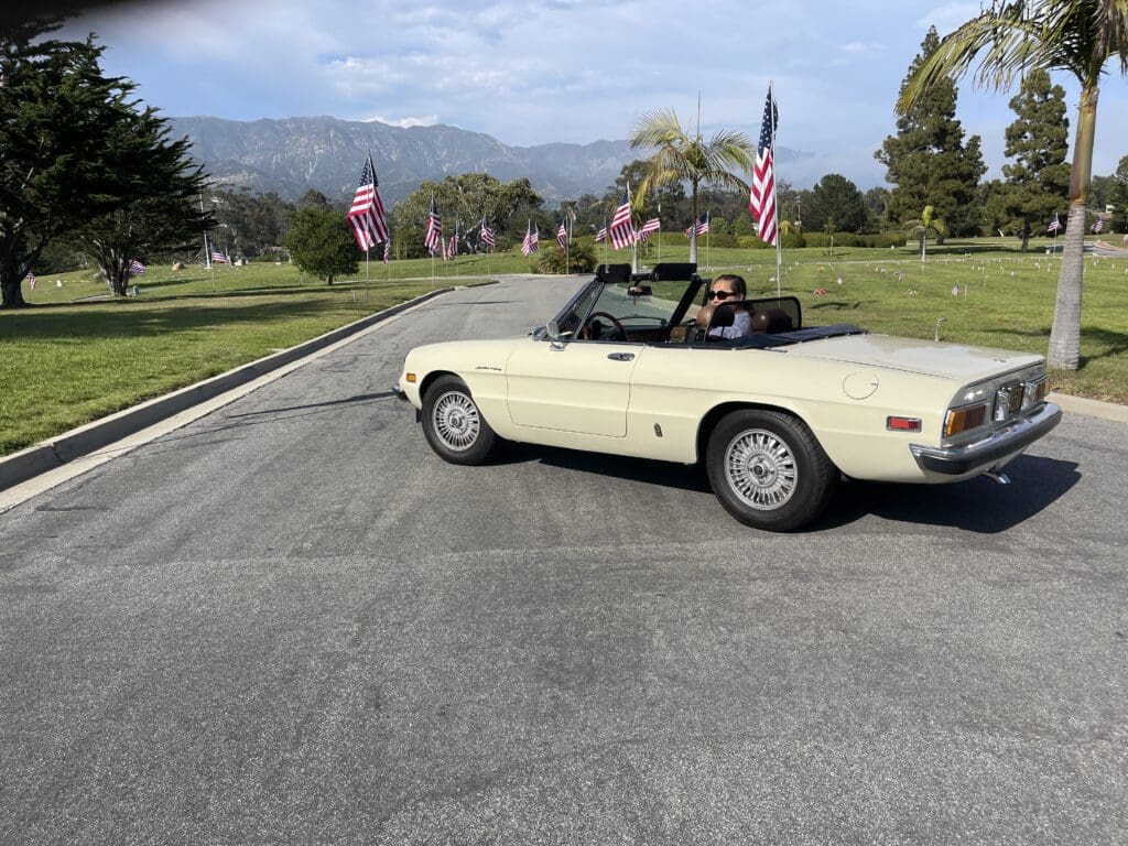 A vintage convertible car on a paved road with mountains in the background.