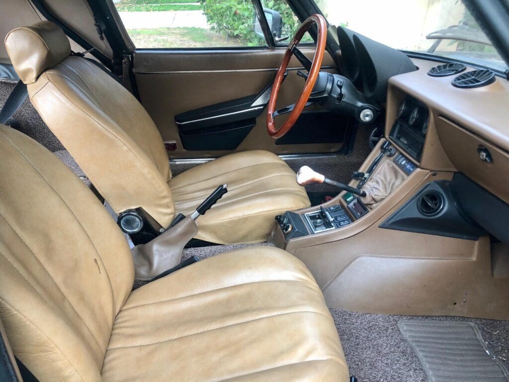 Interior of a vintage car with beige leather seats and wooden steering wheel.