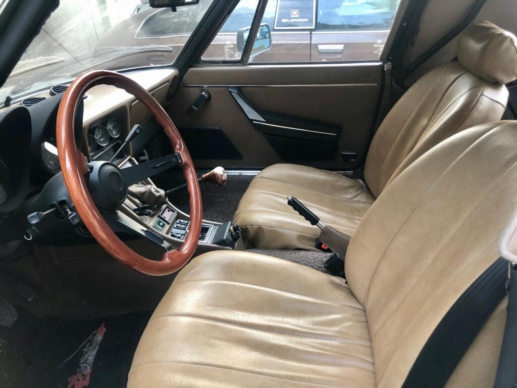 Classic car interior with wooden steering wheel and beige leather seats.