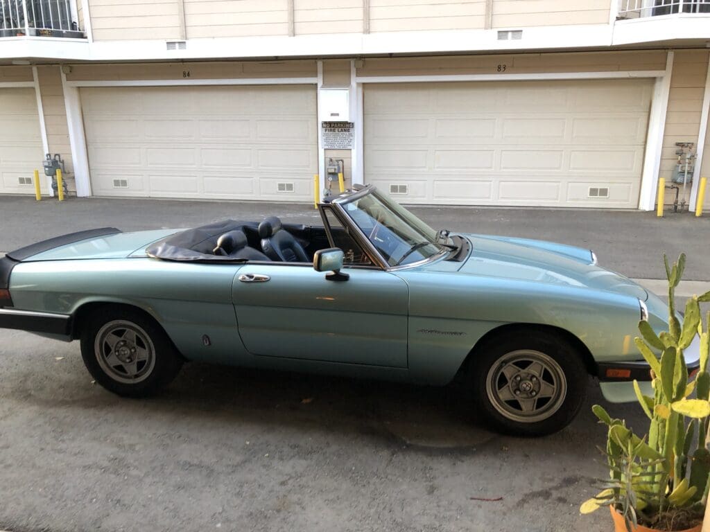 Classic light blue convertible sports car parked in a driveway.