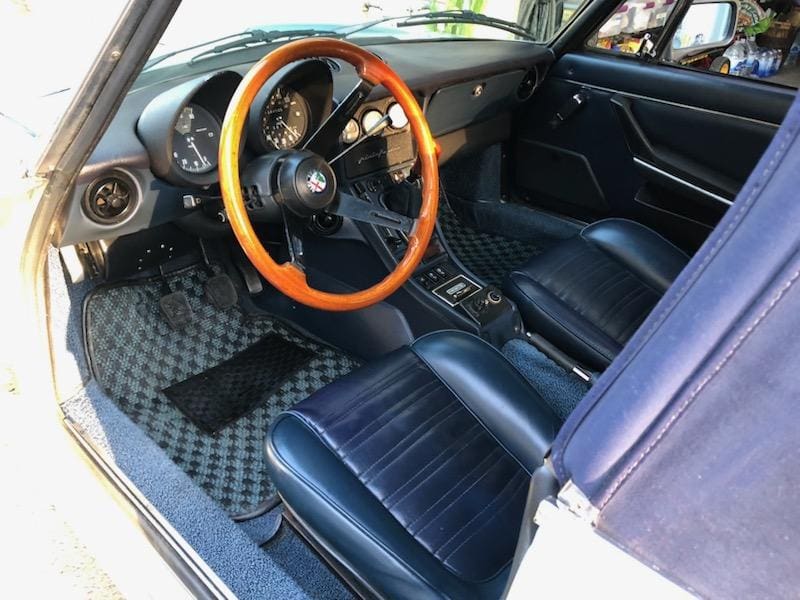 Classic car interior with wooden steering wheel and black leather seats.