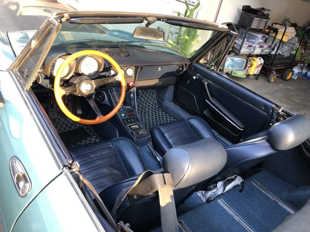 Interior of a vintage convertible car with wooden steering wheel and blue leather seats.
