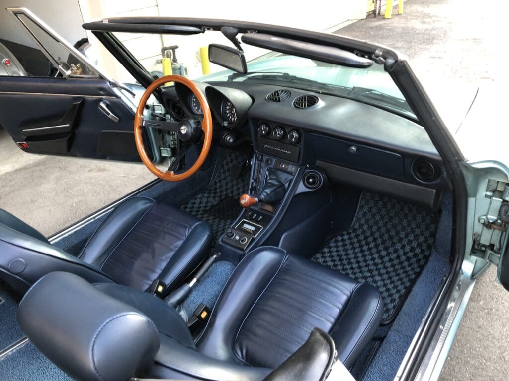Interior of a classic convertible car with wooden steering wheel and black leather seats.