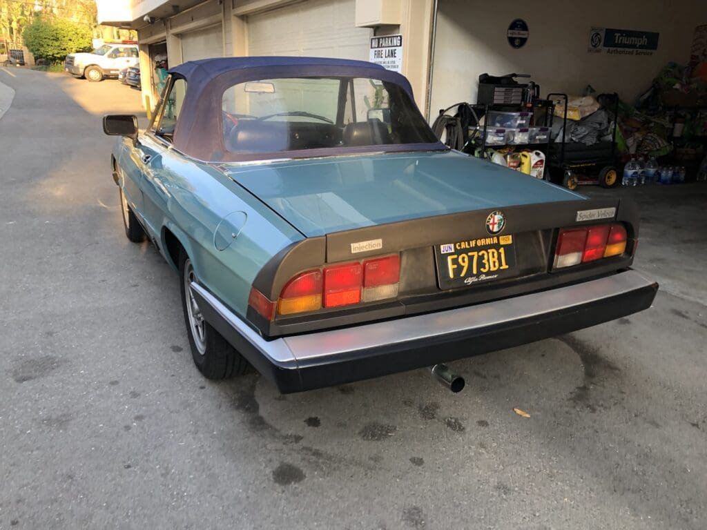 Rear view of a vintage blue convertible car with a black soft top.