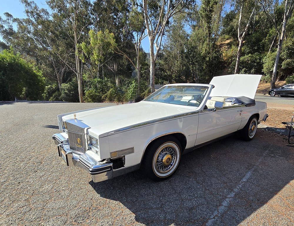 Classic white convertible car with hood open, parked outdoors.