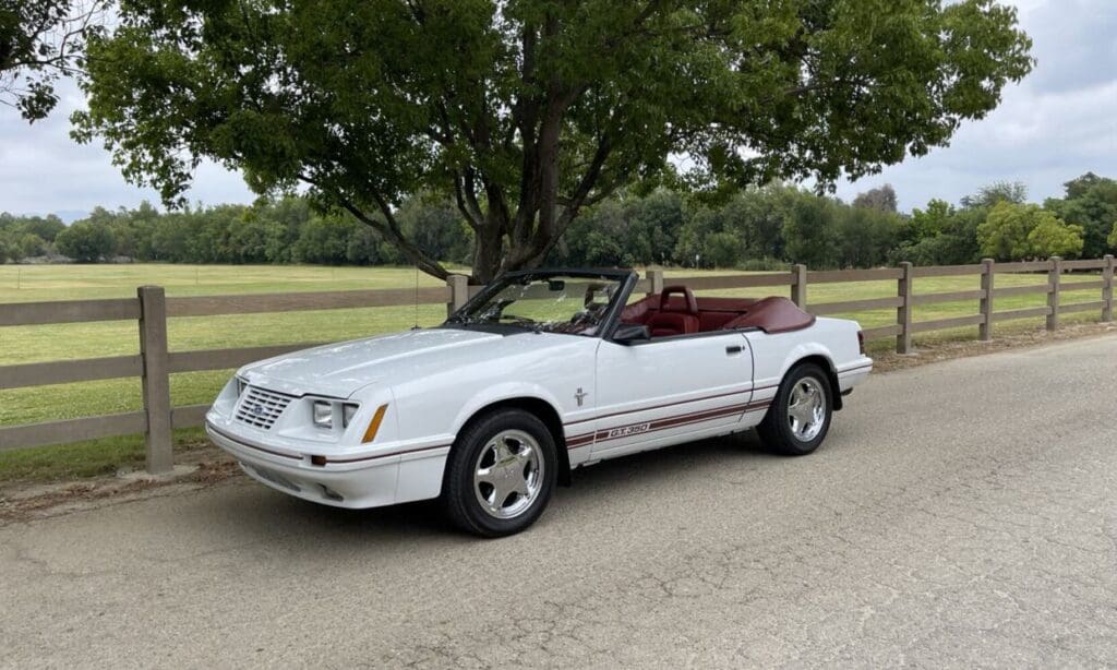 Classic white convertible car parked by a tree on a quiet road.