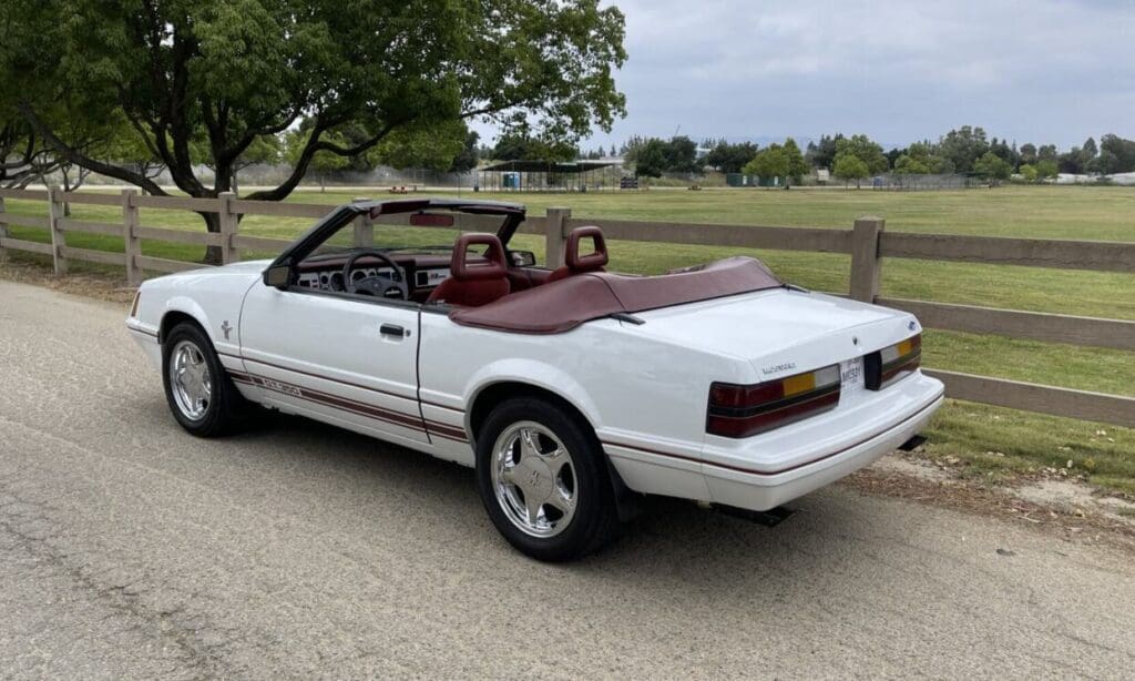 White convertible car with a maroon interior parked outdoors under cloudy skies.