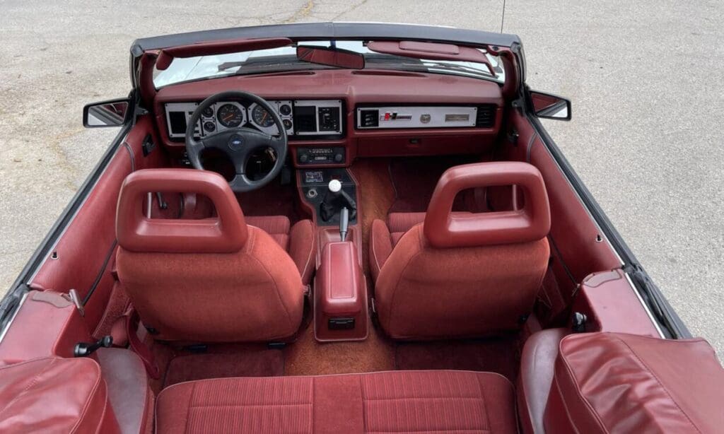 Vintage red interior of a convertible car with detailed dashboard and steering wheel.