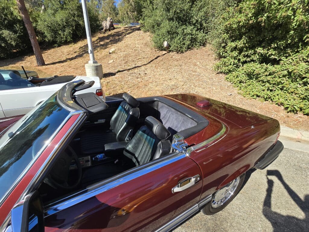 Classic red convertible car parked outdoors with trees in background.