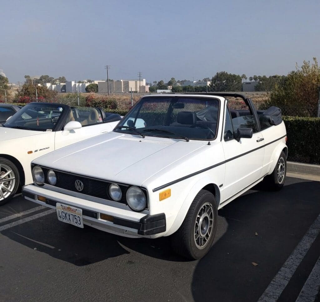 A white vintage convertible car parked in a lot on a sunny day.